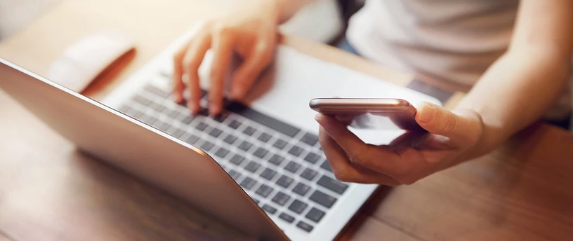 Kvinde sidder med computer og mobiltelefon