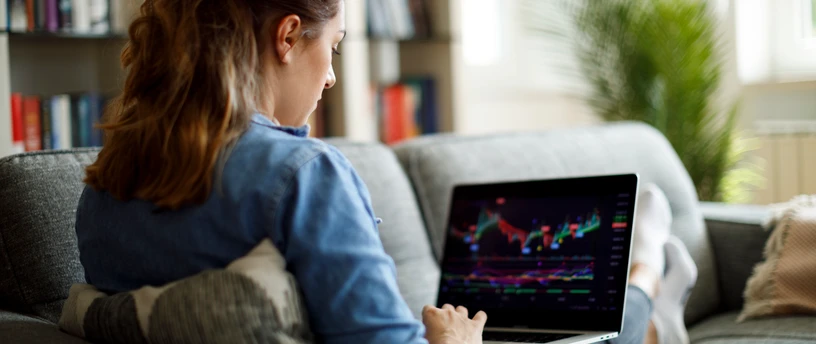 Kvinde tjekker aktier på sin computer i sofaen